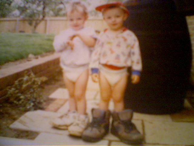 Picture of Luke and Ellis as twins, wearing rather large shoes.